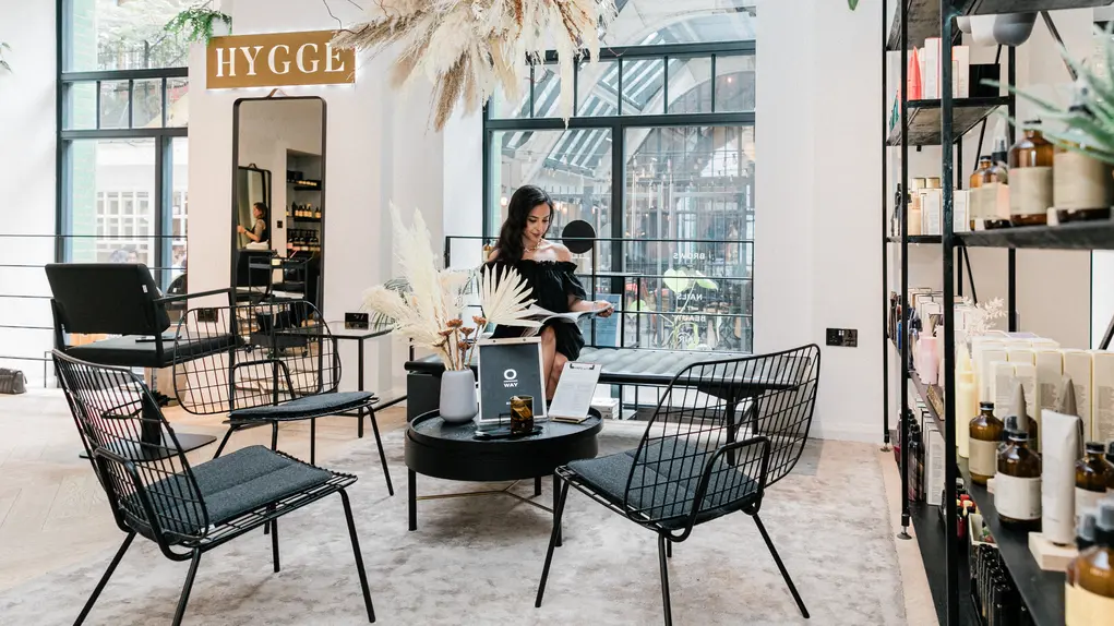 A woman sits in a beauty salon with a sign saying 'Hygge' in the background