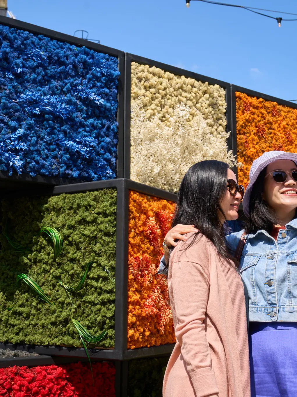 Two women take a selfie in front of a Rubik's cube flower display