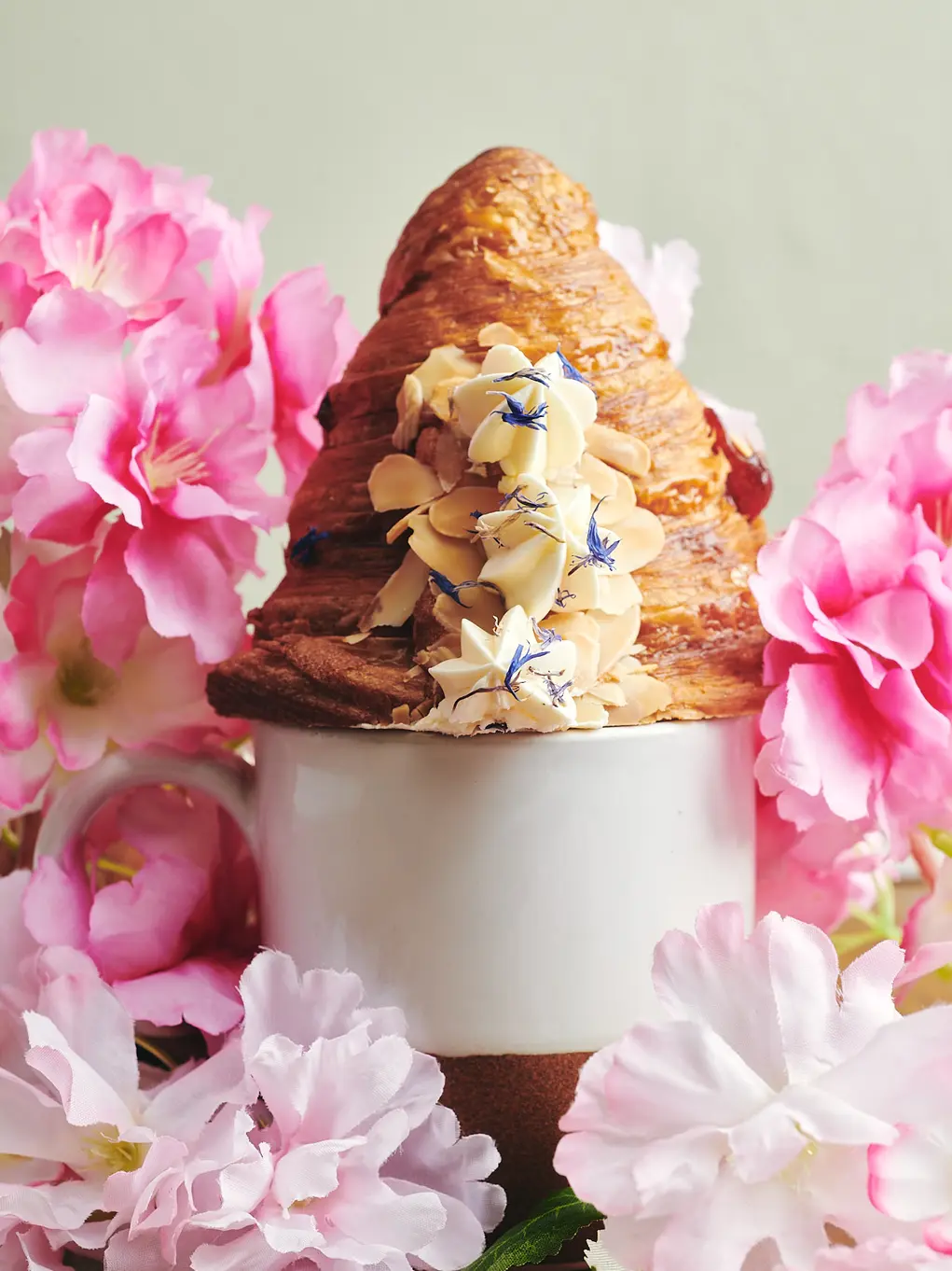 A croissant in a mug surrounded by pink flowers