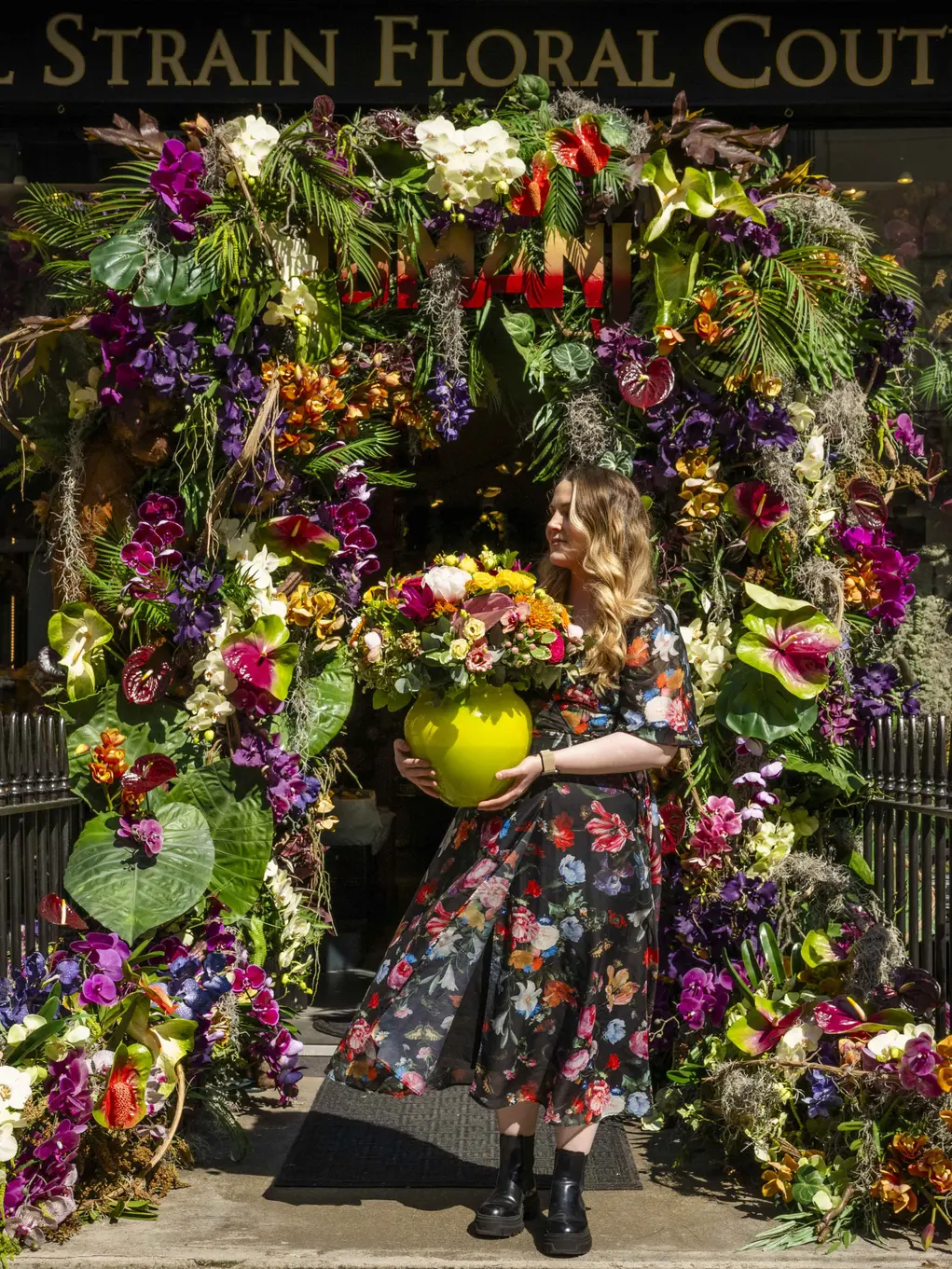 A woman in a floral dress stands outside the Neill Strain Floral Couture shop with its floral display