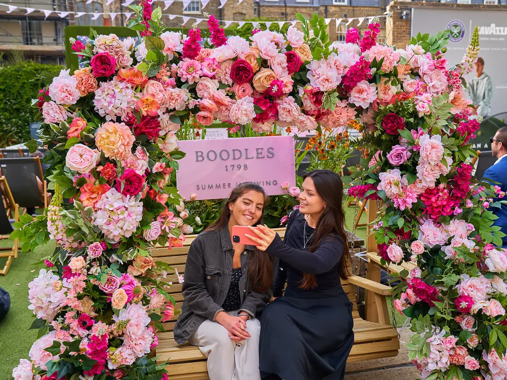 Two women sit on a picnic bench with a floral archway